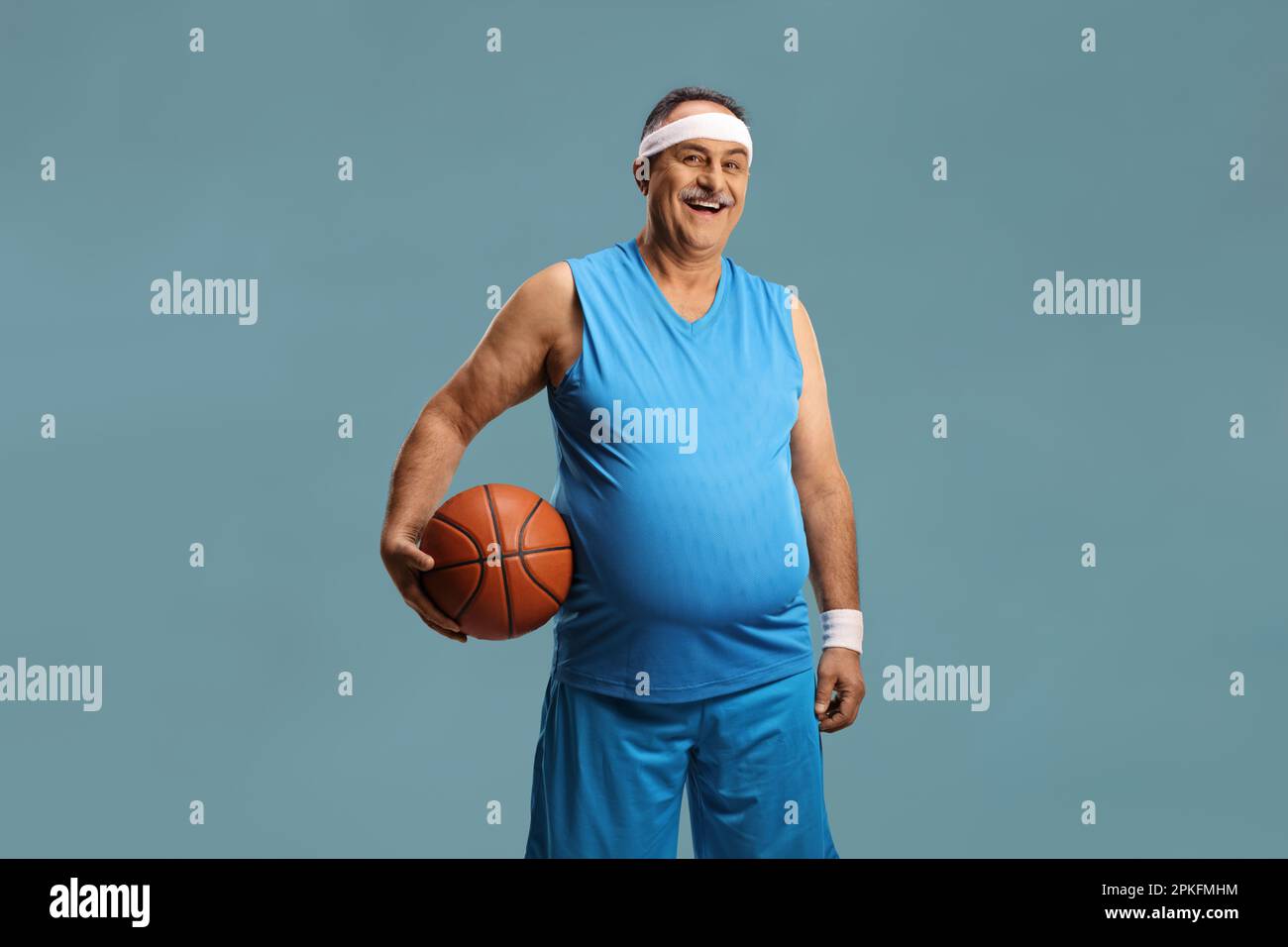 Smiling mature man in a blue jersey holding a basketball isolated on blue background Stock Photo