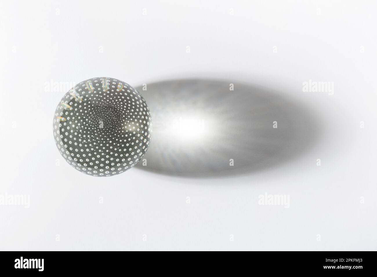 Decorated disco ball with spots on surface made of glass casting large shadow against white backdrop Stock Photo