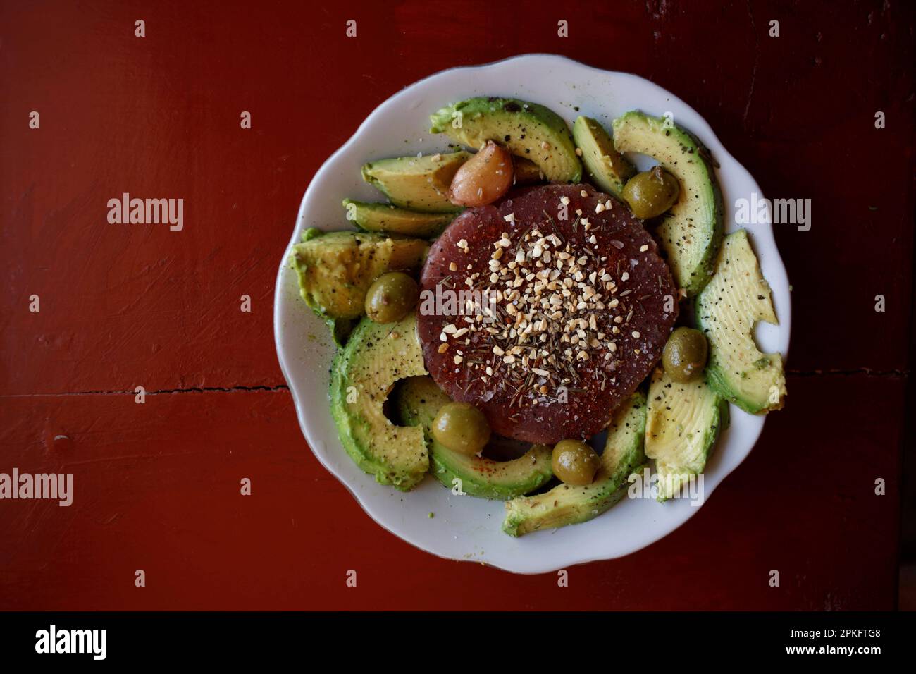 Raw tuna with garlic surrounded by avocado in a plate in a red table in a kitchen in Queretaro, Mexico Stock Photo