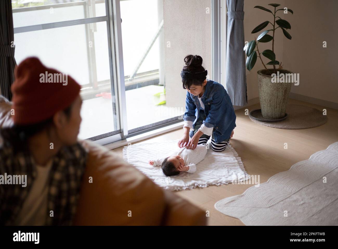 An older sister taking care of her baby brother, while her father watches on Stock Photo