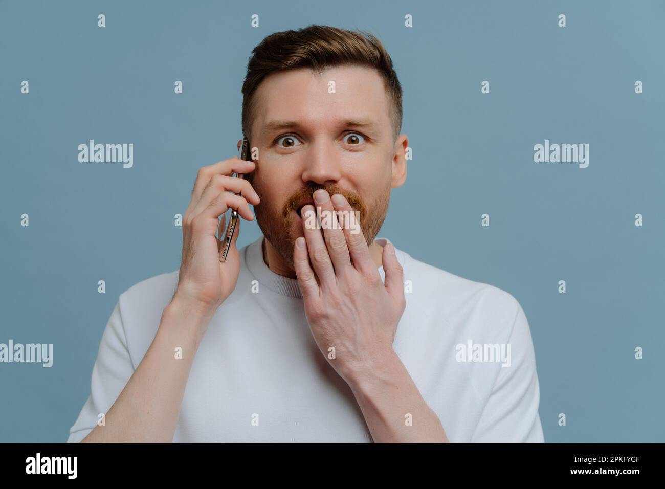 Astonished surprised bearded adult man covers mouth looks with