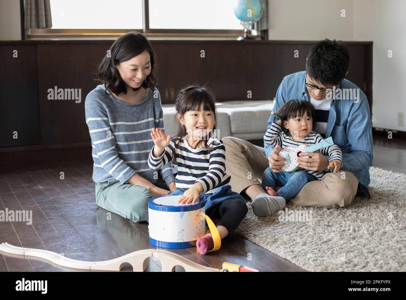 Sisters playing with handmade musical instrument toy and their parents watching Stock Photo
