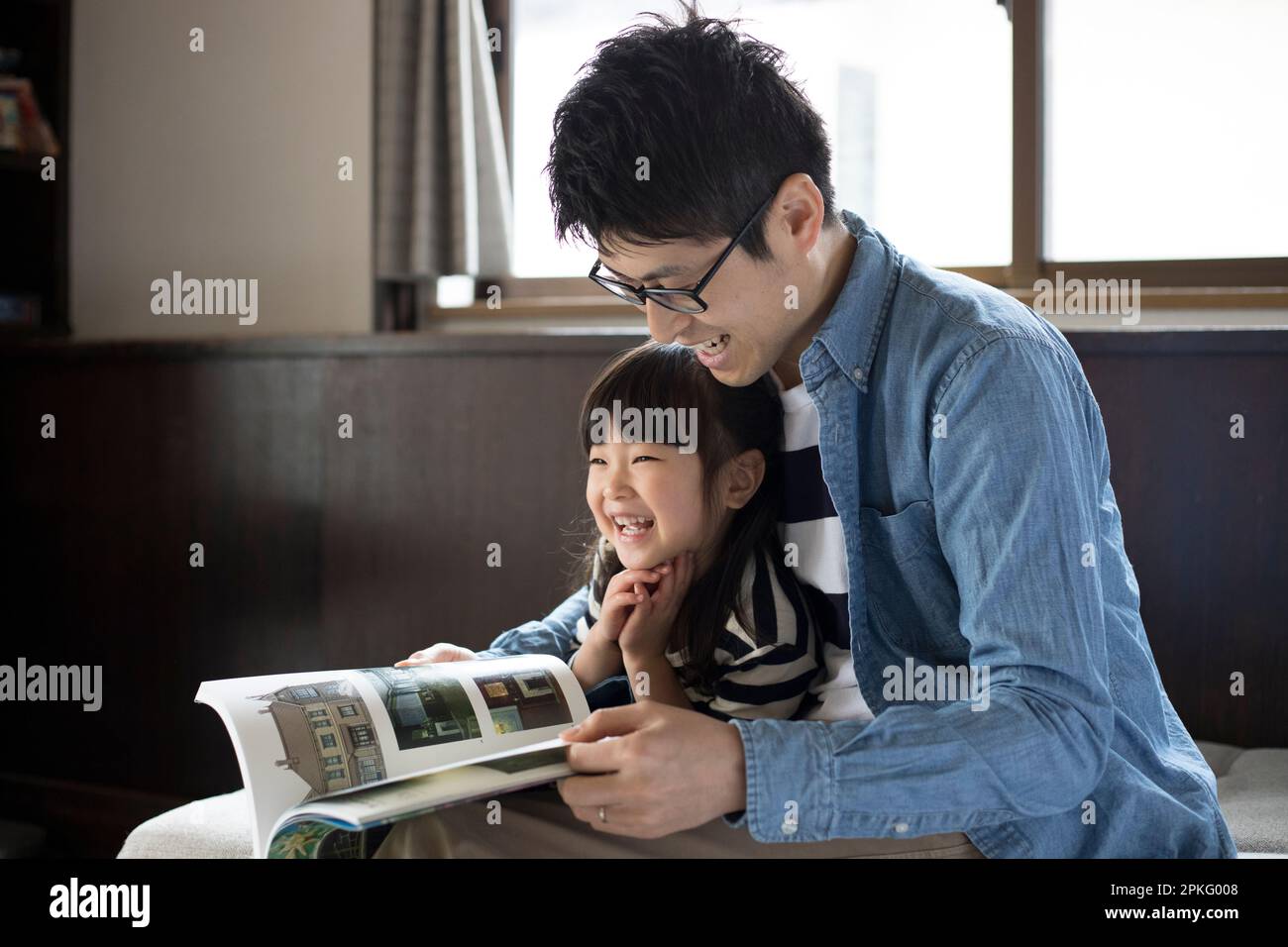 Girl sitting on her father's lap and having a book read to her Stock Photo