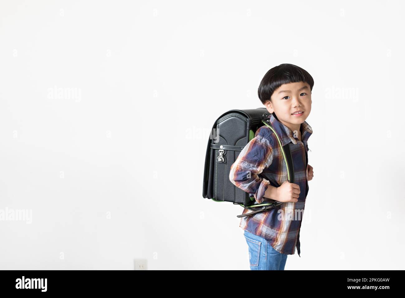 An elementary school boy standing in front of a white wall with his ...