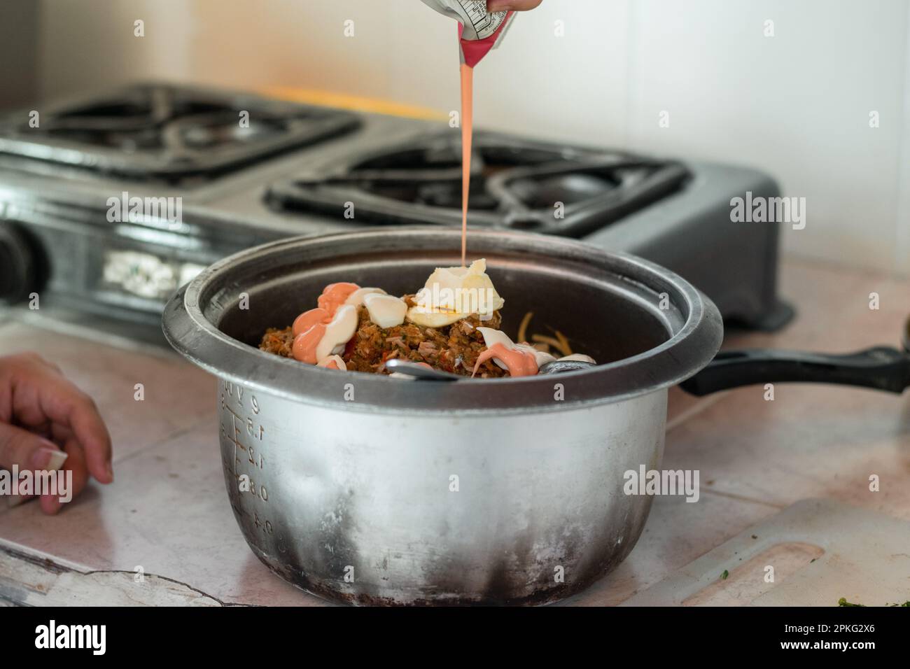 woman pouring pink sauce over the pot with spaghetti Stock Photo