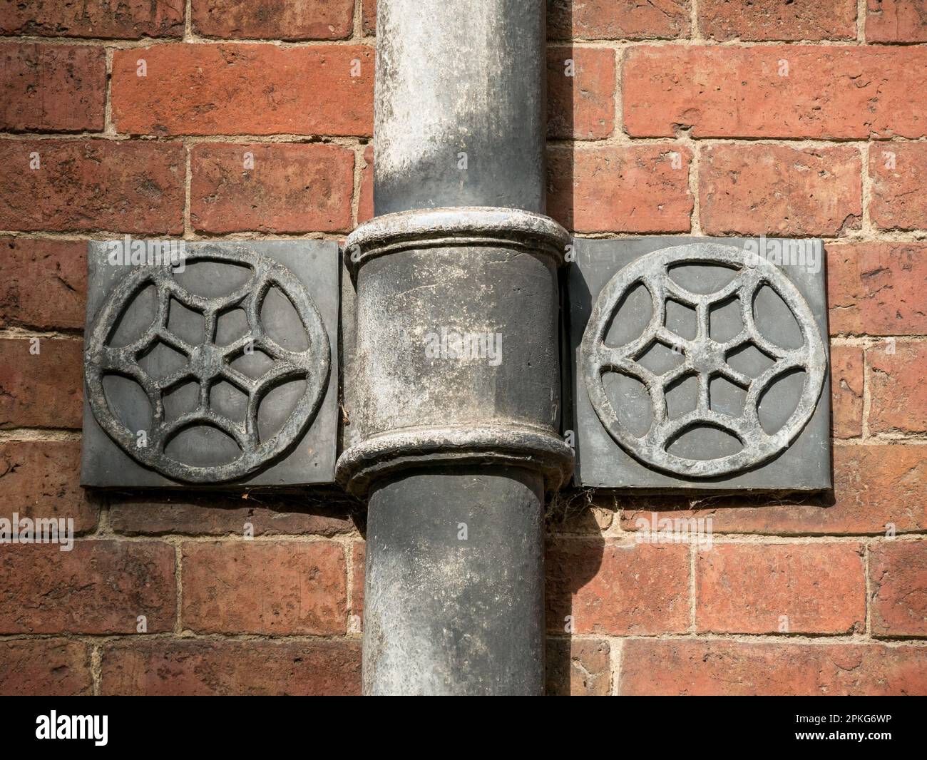 Old ornate lead guttering downpipe support bracket on red brick wall, Calke Abbey, Ticknall, Derbyshire, England, UK Stock Photo