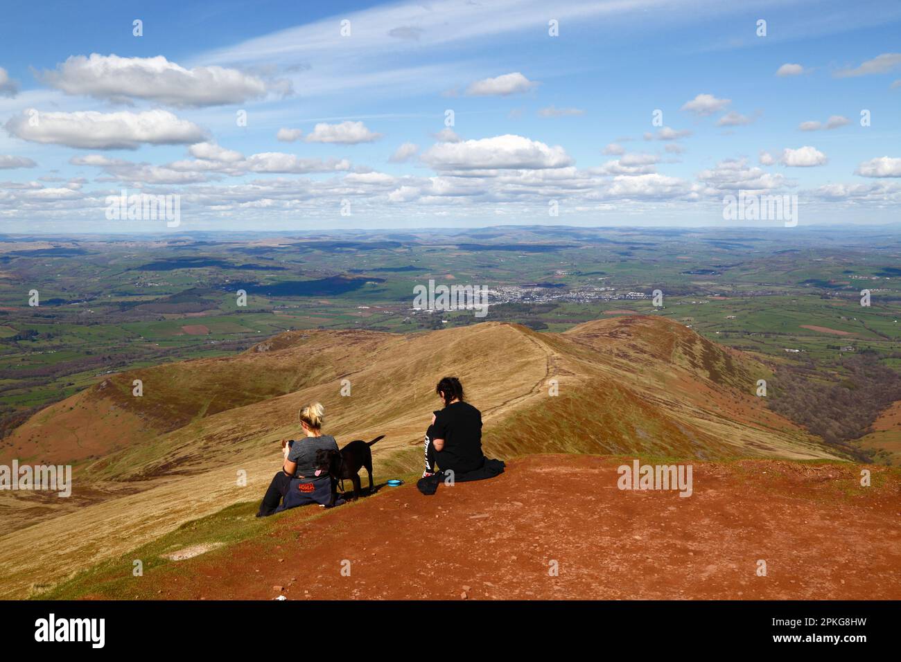 UK Weather: Good Friday bank holiday, April 7th, 2023. Brecon Beacons National Park, South Wales. Hikers looking at their smartphones on the summit of Pen y Fan in the Brecon Beacons National Park. The town of Brecon is in the distance, the ridge in the centre is Cefn Cwm Llwch, the approach route from the north. Beautiful sunny weather meant many people made the trip to the Park for today's bank holiday. Stock Photo