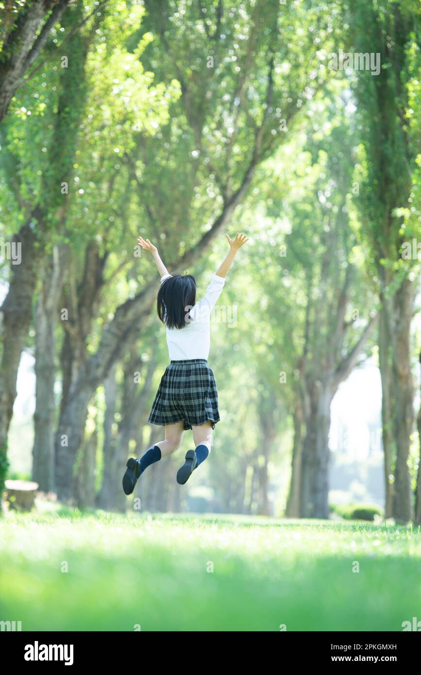 Rear view of a female student jumping on a row of poplar trees Stock ...