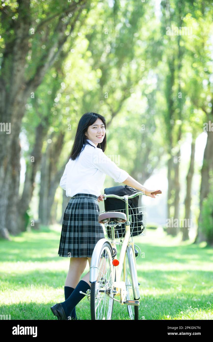 Female student pushing a bicycle along poplar trees Stock Photo