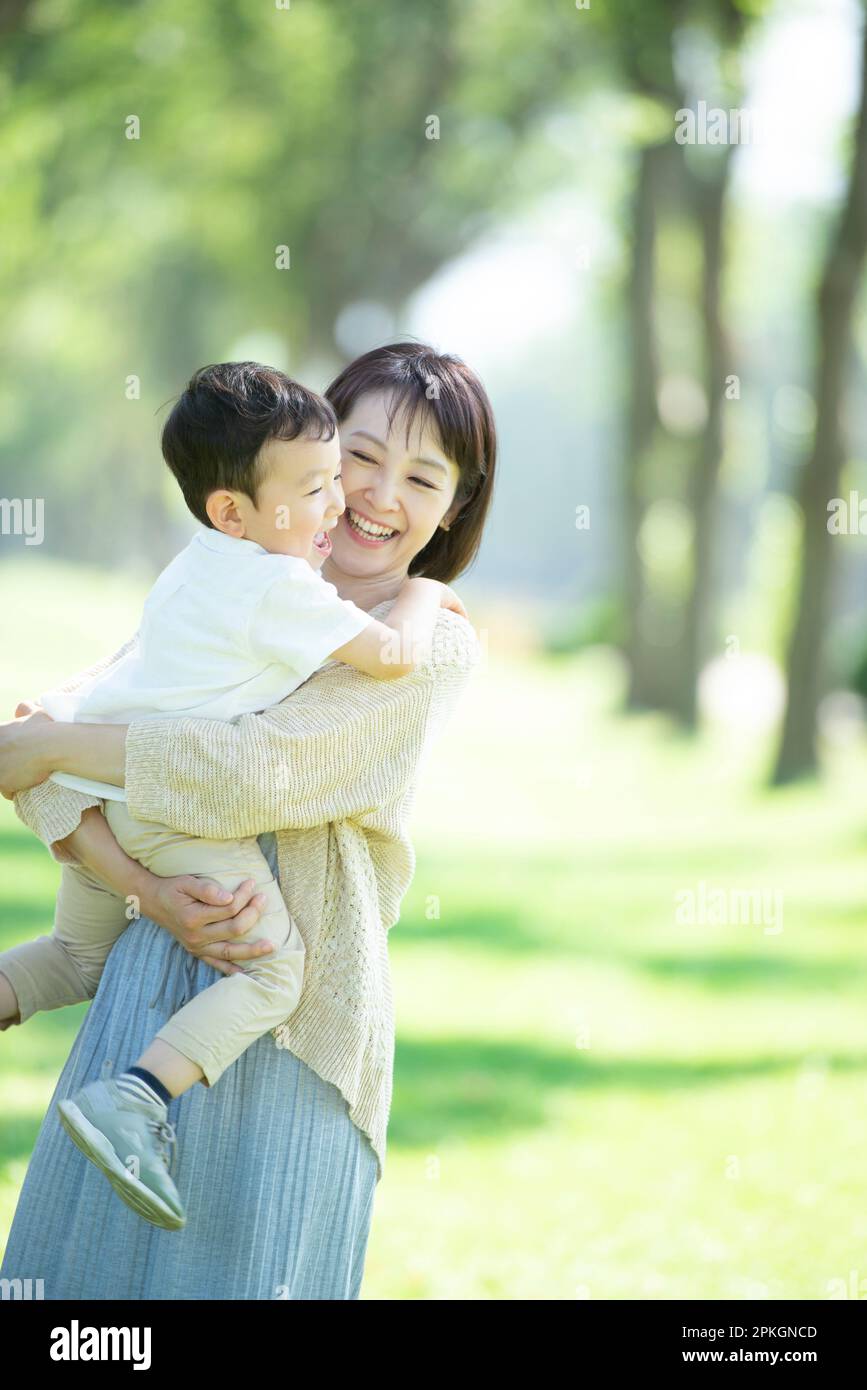 A mother smiles as she holds her child in her arms at a row of poplar trees Stock Photo