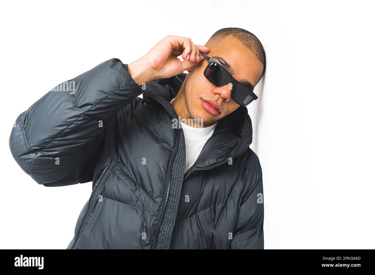 young Afro-Americn man with sunglasses and a winter jacket leaning on a wall, white background studio shot medium. High quality photo Stock Photo