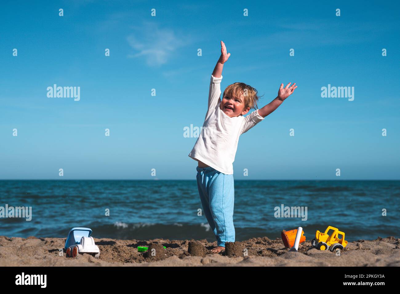 3 year old blond boy plays on the seashore in the sand with toys Stock Photo