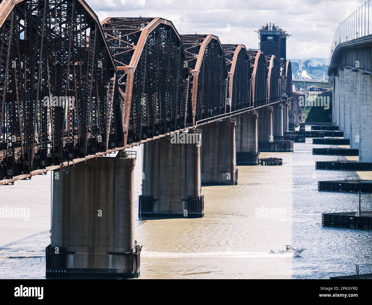 A speed boat passes under Benicia, California's rusty-looking steel railway bridge. Stock Photo