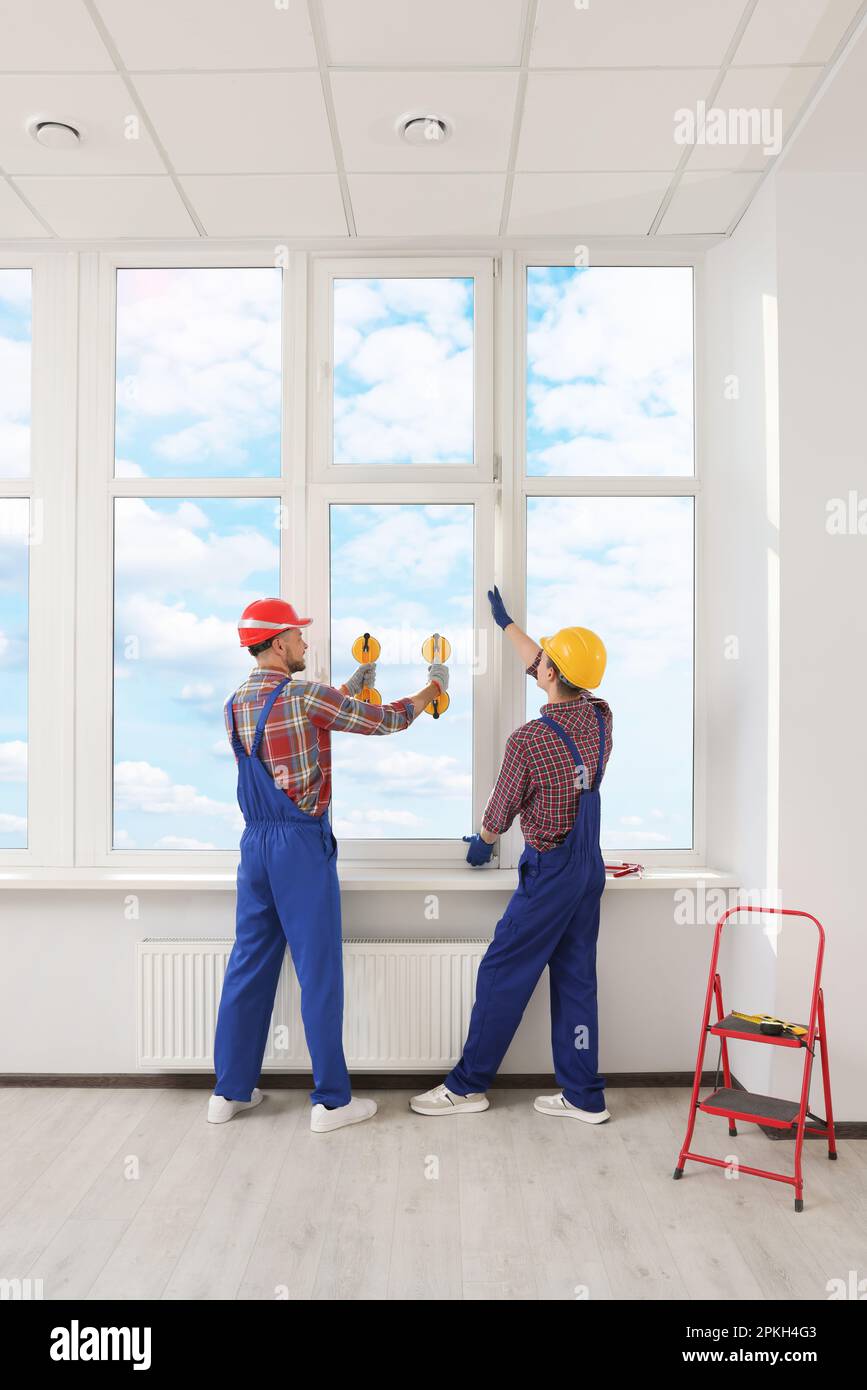 Workers using suction lifters during plastic window installation indoors Stock Photo