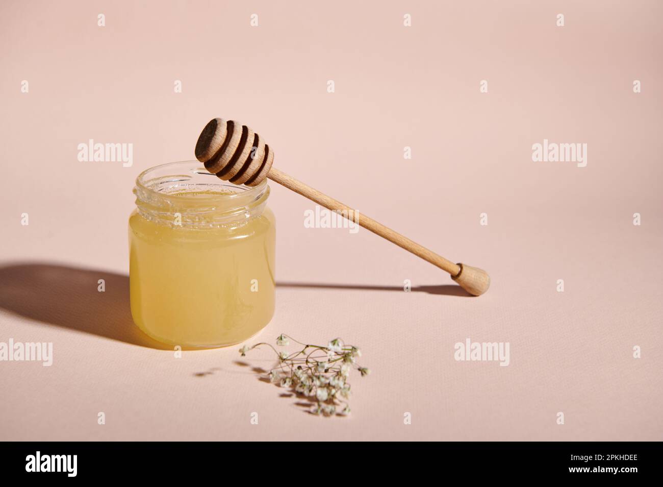 Still Life with wooden dripper on a jar with organic honey and dried bouquet of meadow flowers on pink pastel background Stock Photo