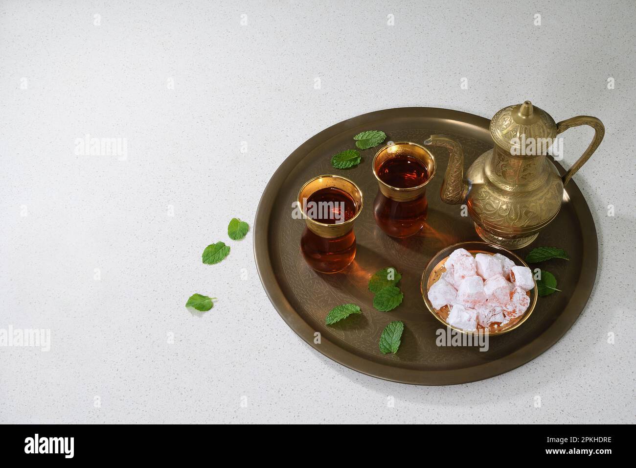 A classic, celebratory, ornate Turkish teapot, two glasses and traditional turkish delights on a tray in soft lighting with copy space to the left Stock Photo