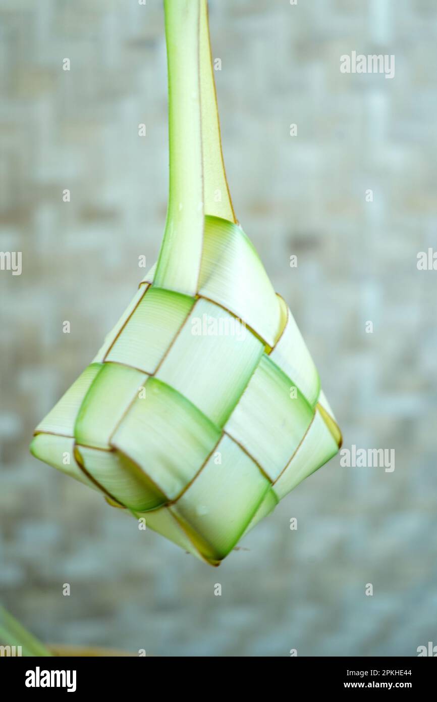 Empty ketupat or empty woven palm leaf hung in a room with woven bamboo wall background. Preparation for Idul Fitri or Eid Mubarak in Indonesia. Copy Stock Photo