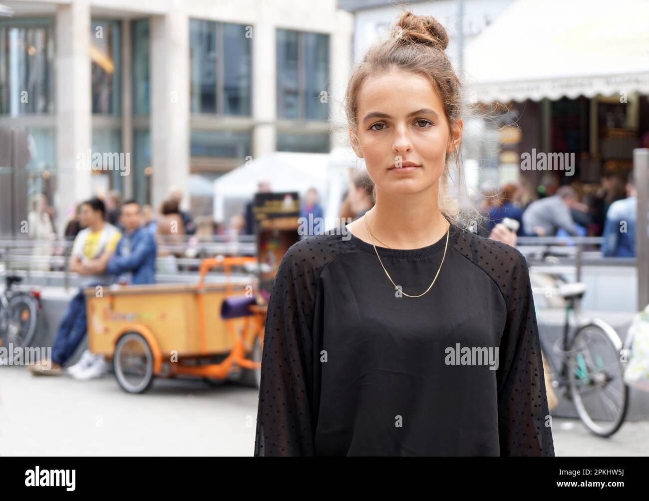young woman downtown in a pedestrian area with blurred people and shops in the background Stock Photo