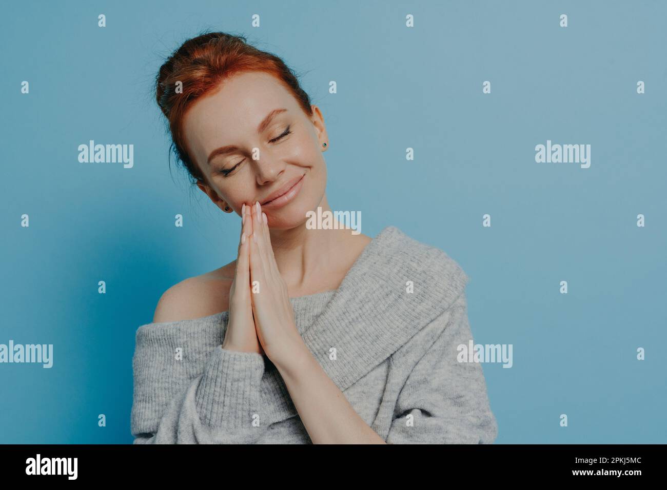Happy calm redhead grateful woman holding hands in prayer gesture with closed eyes and tilted head, waiting for miracle with smile on face isolated on Stock Photo