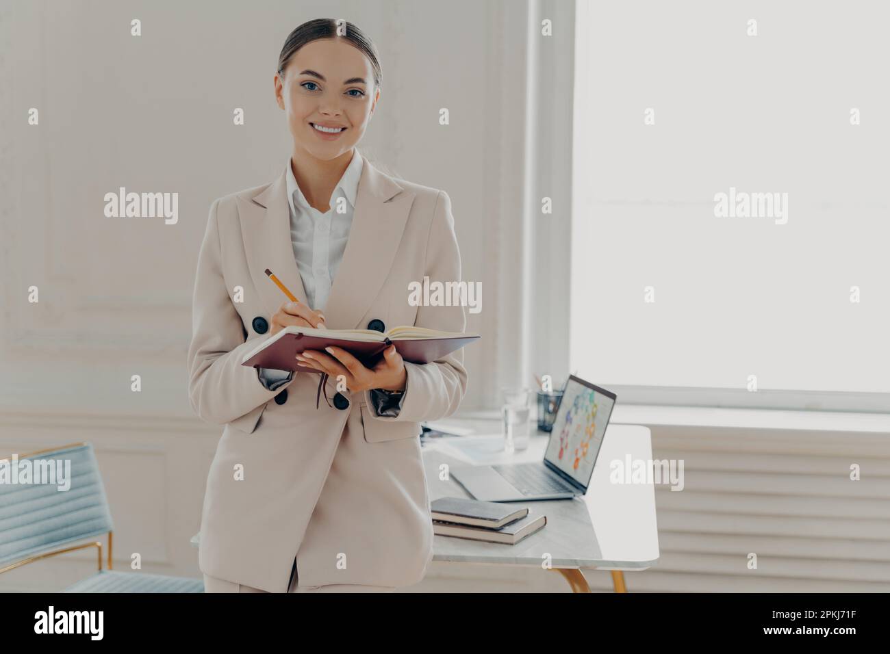 Positive happy female director in elegant wear planing working day, being in good mood while standing in modern light office interior, happy businessw Stock Photo