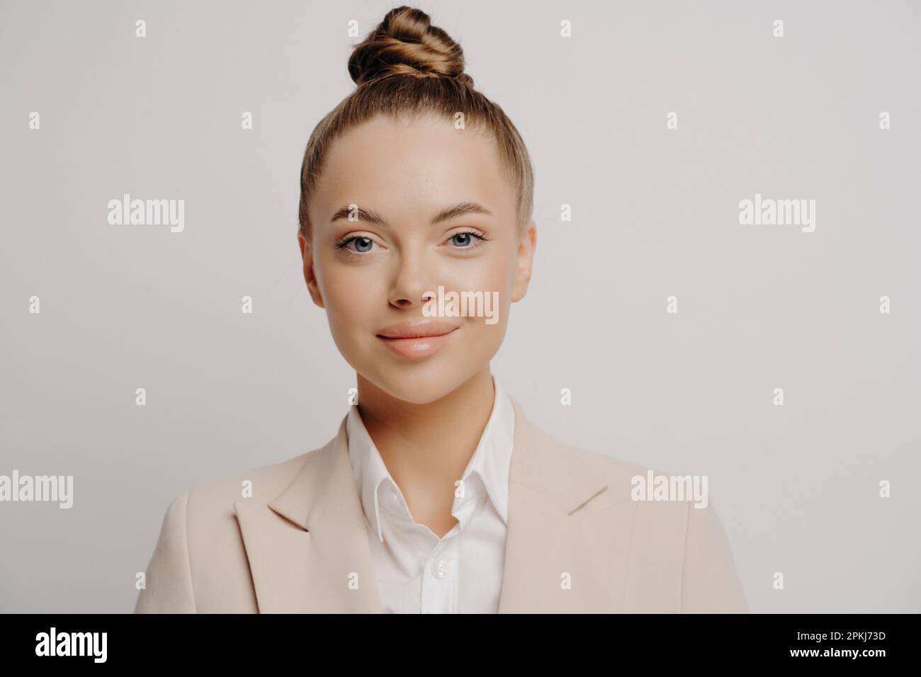 Close up portrait of young pretty brunette business lady with hair bun wearing formal clothes with white shirt standing isolated in front of grey back Stock Photo