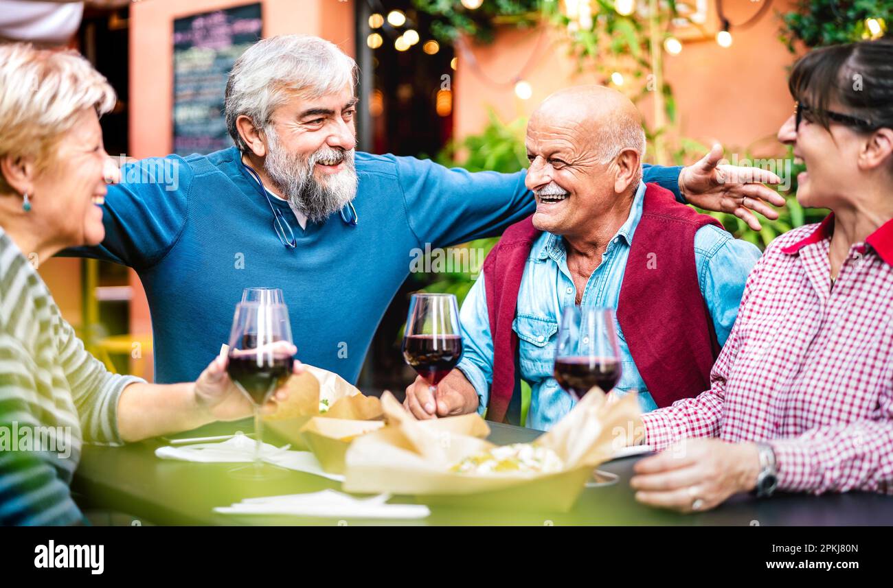 Genuine retired people having fun drinking red wine at dinner party - Senior friends eating together outside at restaurant - Dinning life style concep Stock Photo