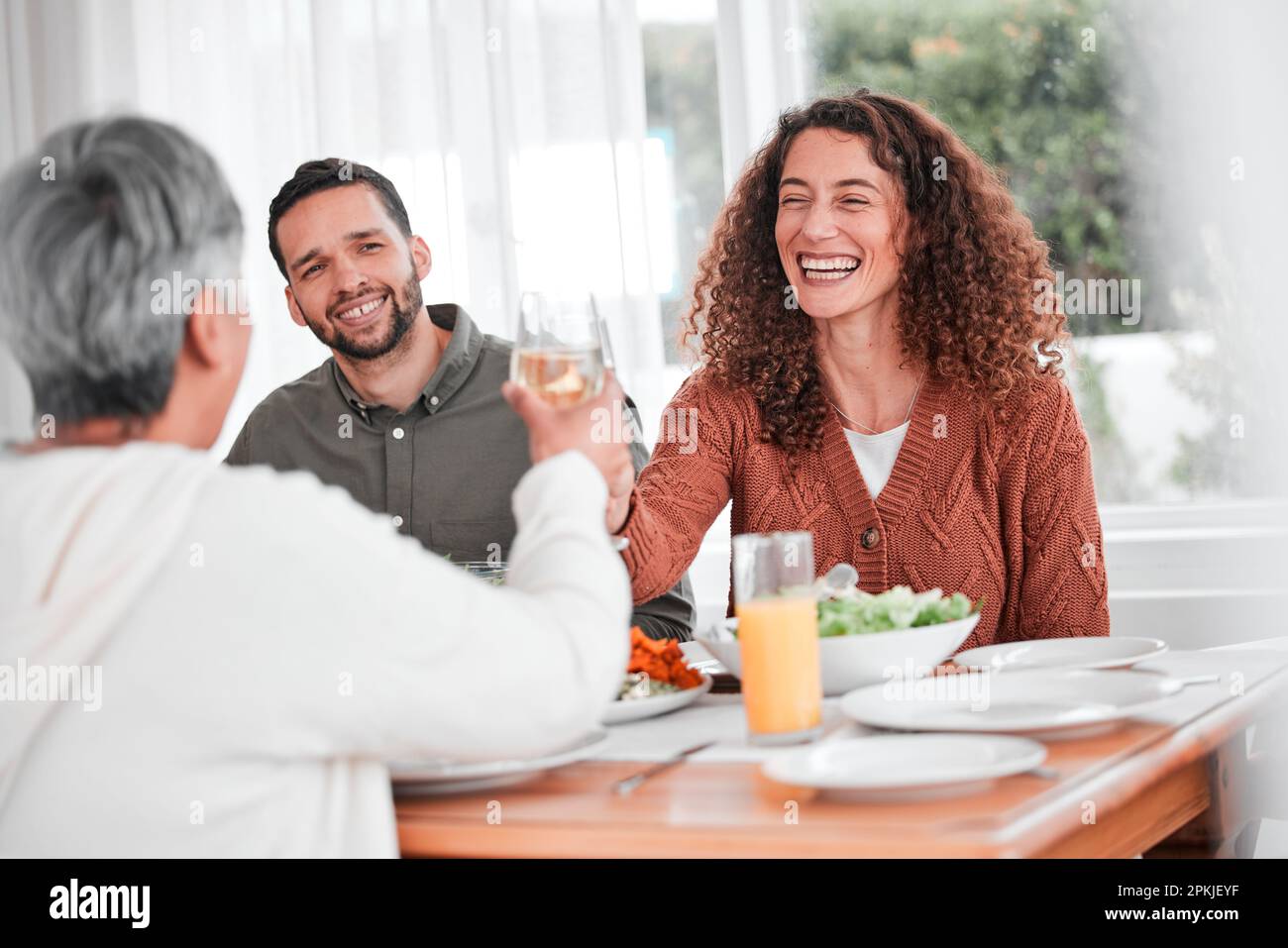 Family dinner, couple and cheers of a happy woman with healthy food in a home. Celebration, together and people with unity from eating at table with Stock Photo
