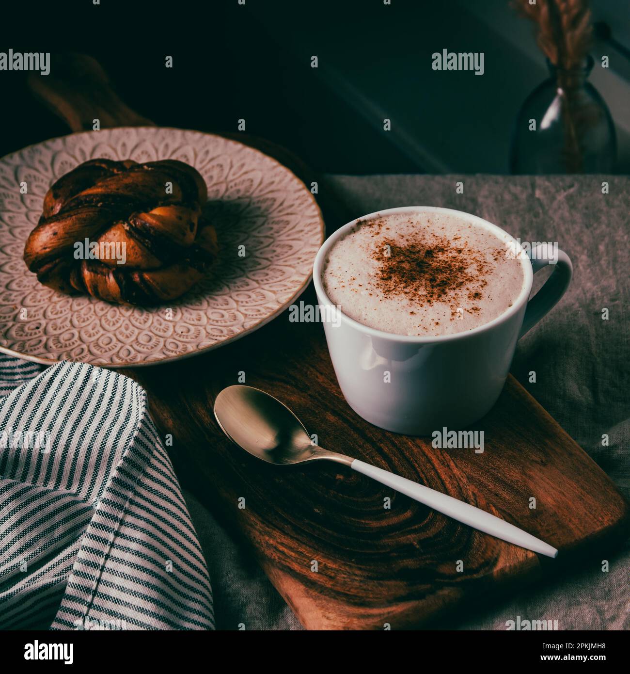 Cinnamon bun with a cup of cappuccino and a golden spoon on a wooden board Stock Photo