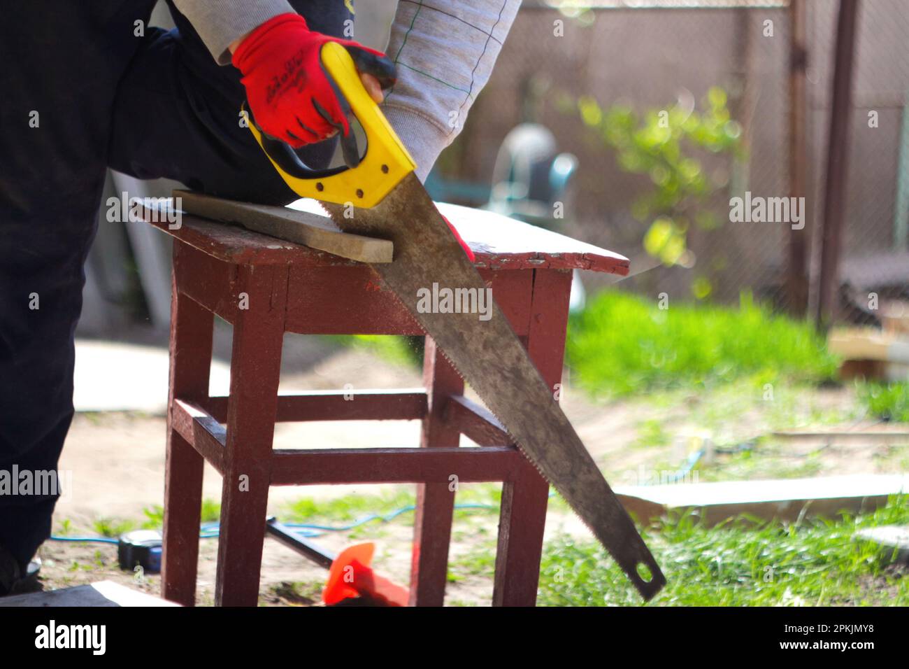 Man cut with yellow saw outside. Defocus saw on blurred background. Closeup handle yellow saw. Out of focus. Stock Photo