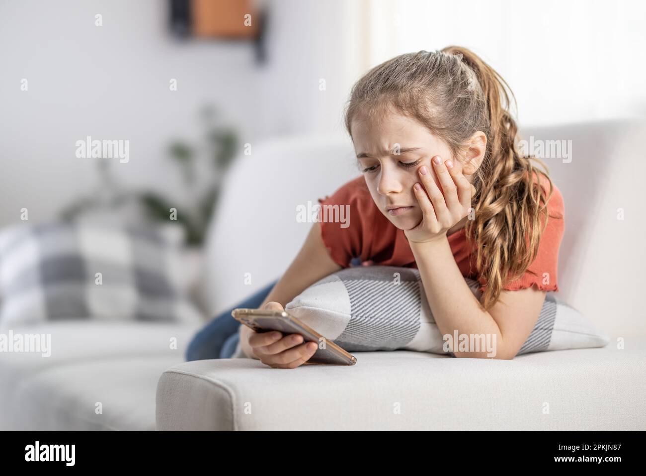 Bored young girl finds no more joy in scrolling on her phone as she sits at home on a couch. Stock Photo
