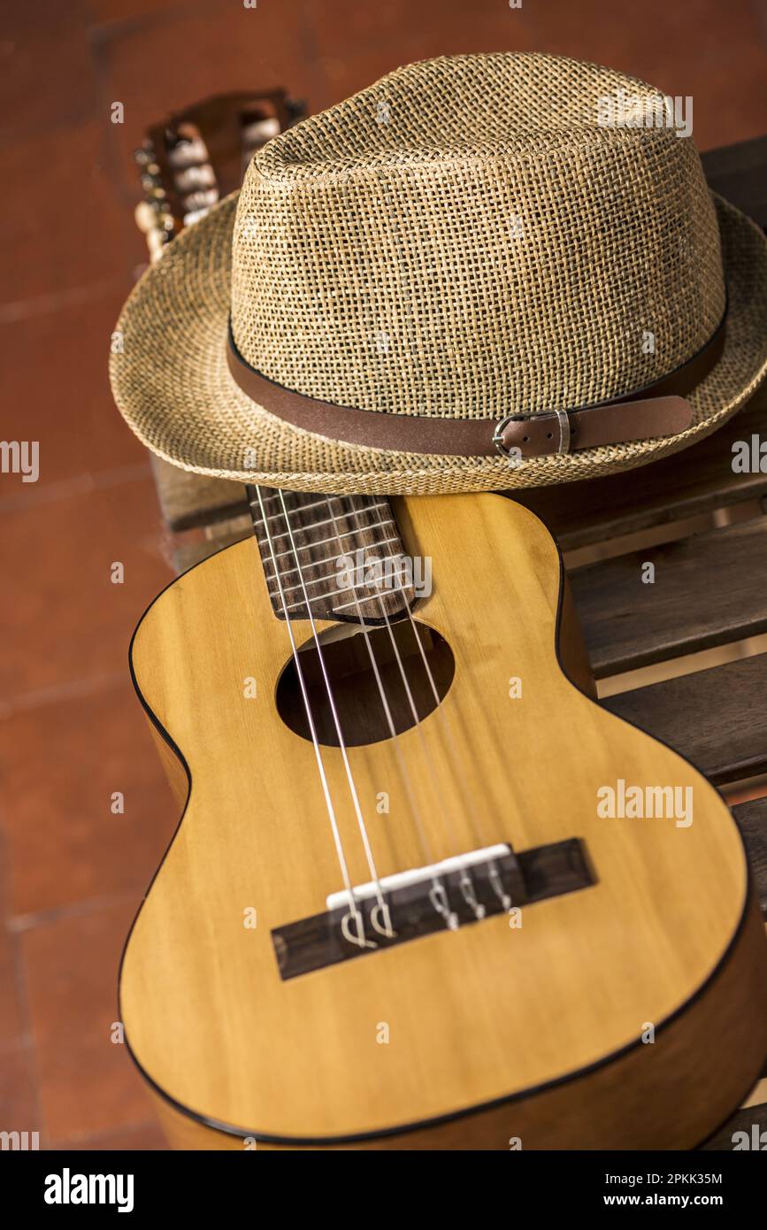 A guitar resting on a wooden box and a straw hat and clay flooring Stock Photo