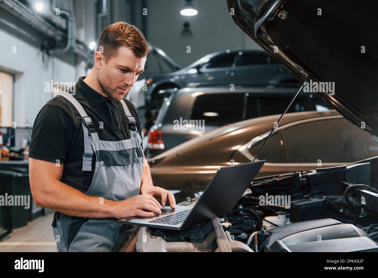 Using laptop. Man in uniform is working in the auto service Stock Photo