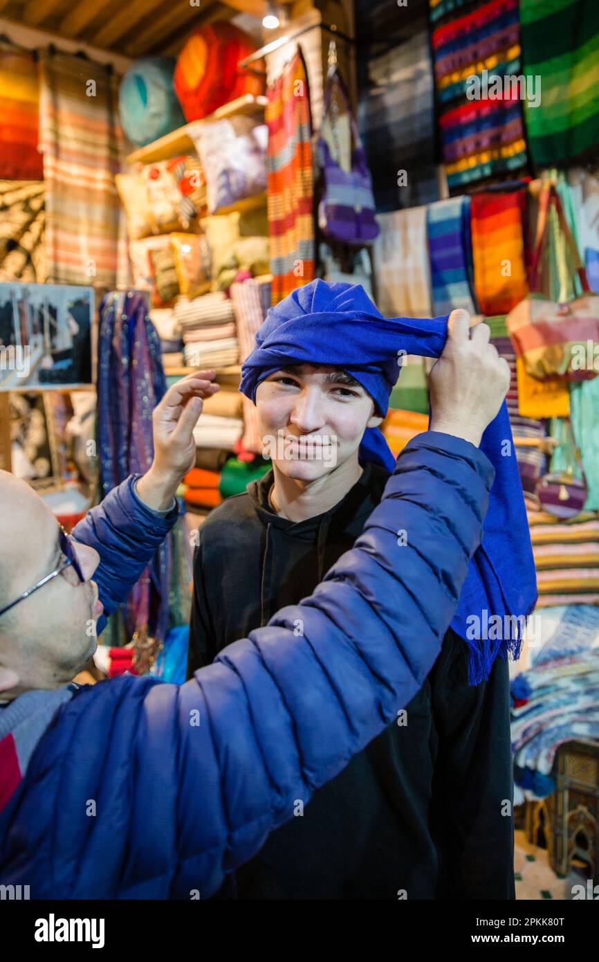 A man ties a tuareg headscarf on an American teen boy tourist in Fez Medina Morocco Stock Photo