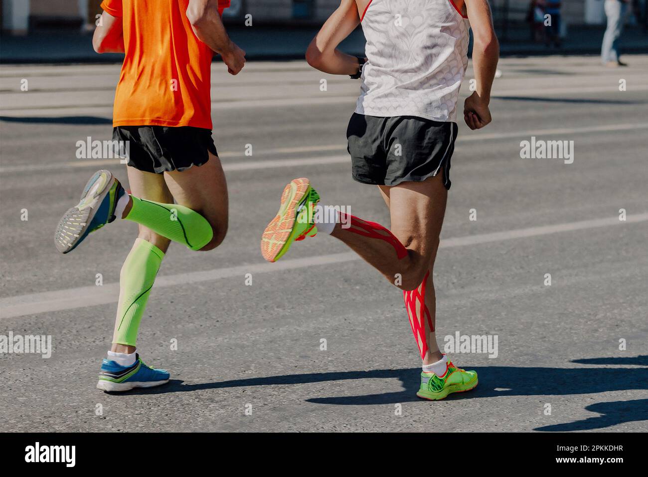 back two athletes runners running marathon in city, legs man jogger in compression sleeves and kinesiotaping calf muscle Stock Photo