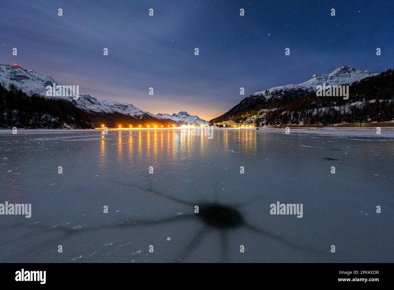 Holes in the cracked ice on Lake Champfer with Silvaplana village on ...