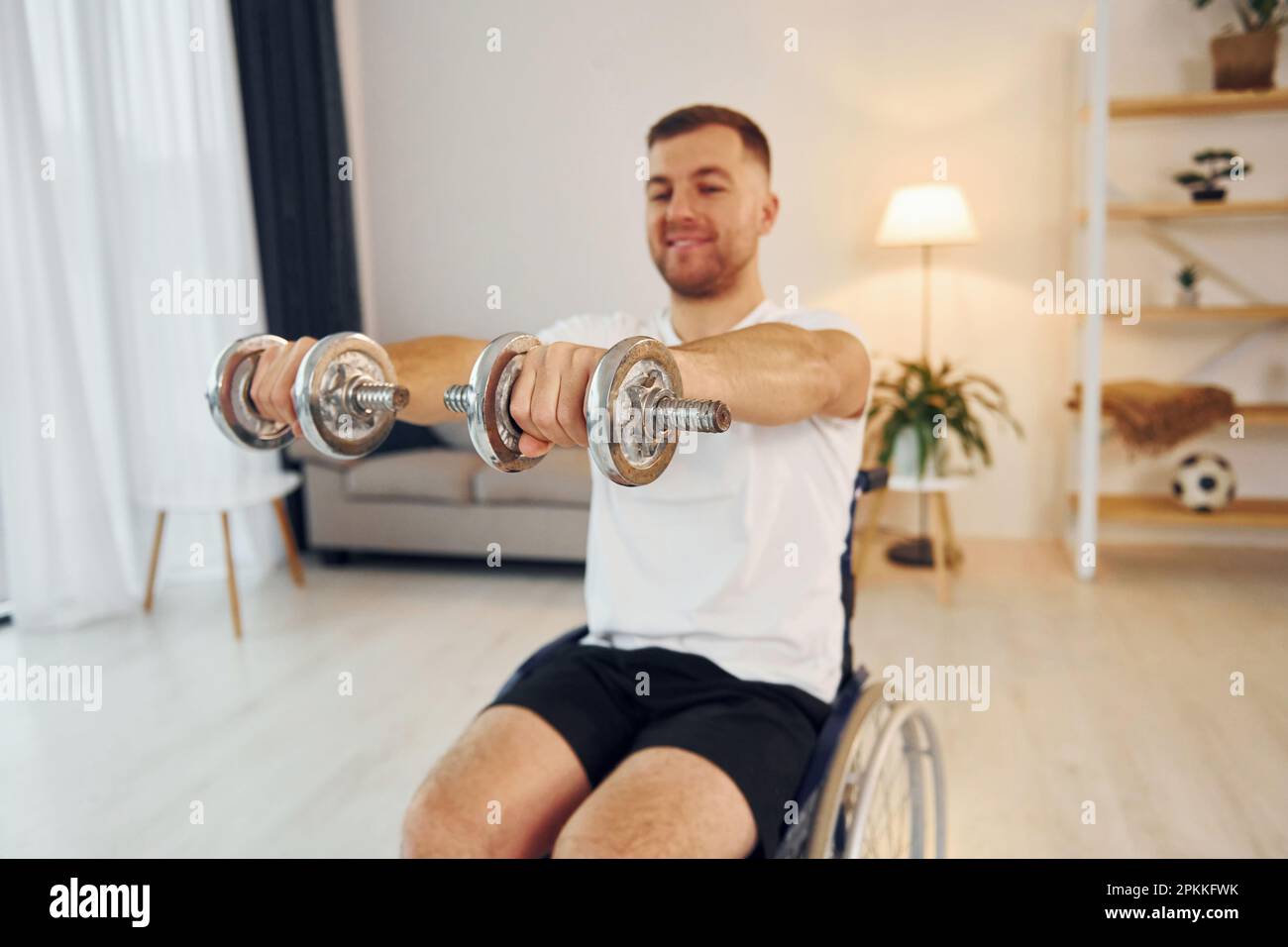 Doing exercises by using dumbbells. Disabled man in wheelchair is at ...