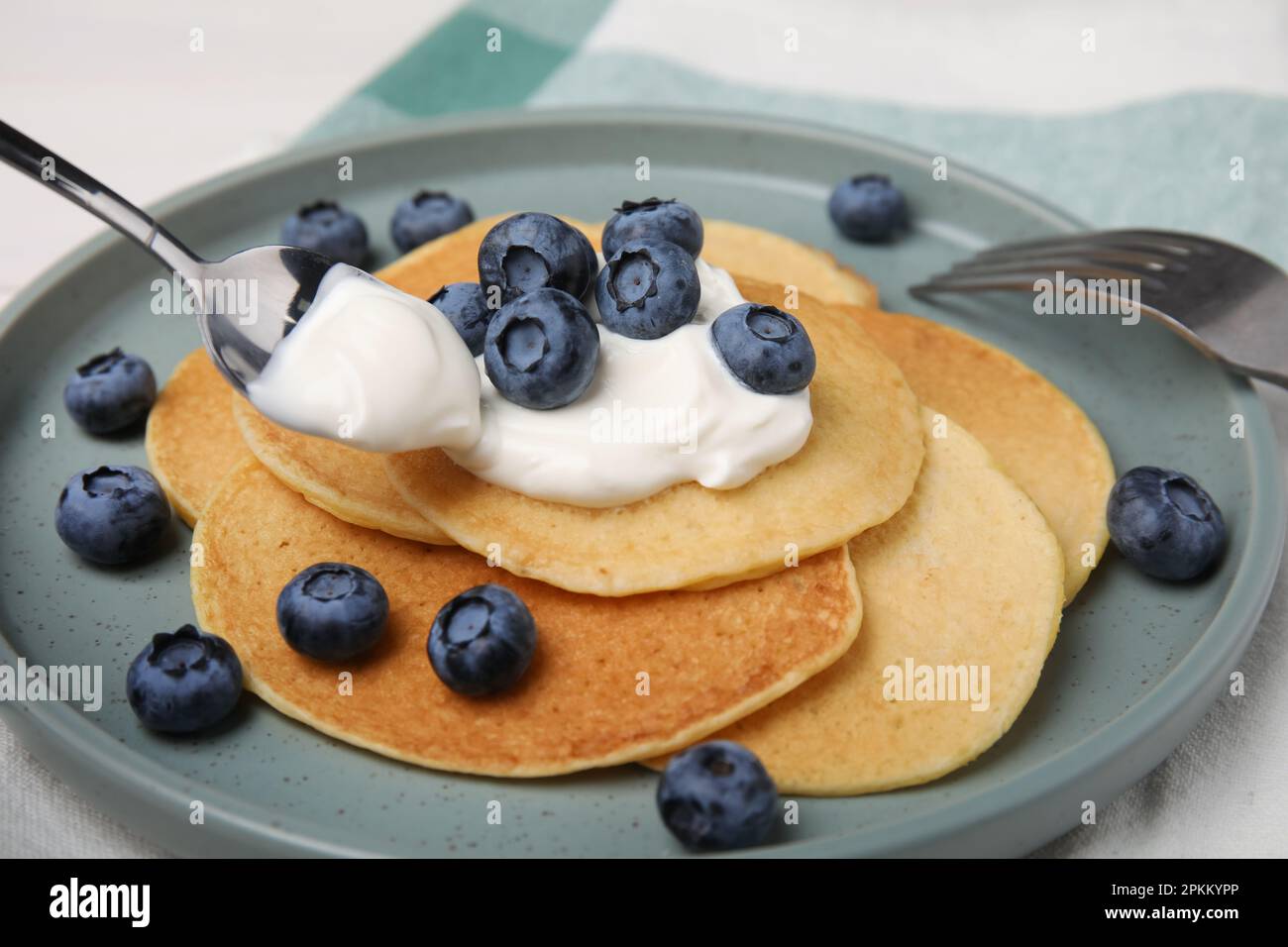 Putting natural yogurt onto tasty pancakes with blueberries at table, closeup Stock Photo