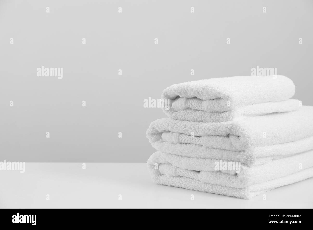 Stack of clean soft white towels on table against light grey background