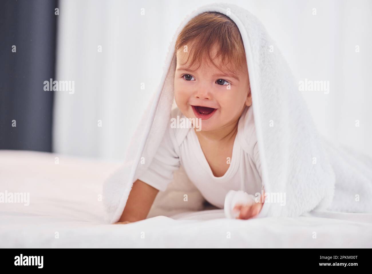 With white towel. Cute little baby is indoors in the domestic room. Stock Photo