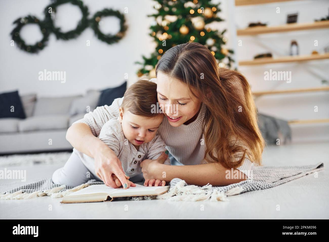 Sitting on the ground. Mother with her little daughter is indoors at home together. Stock Photo