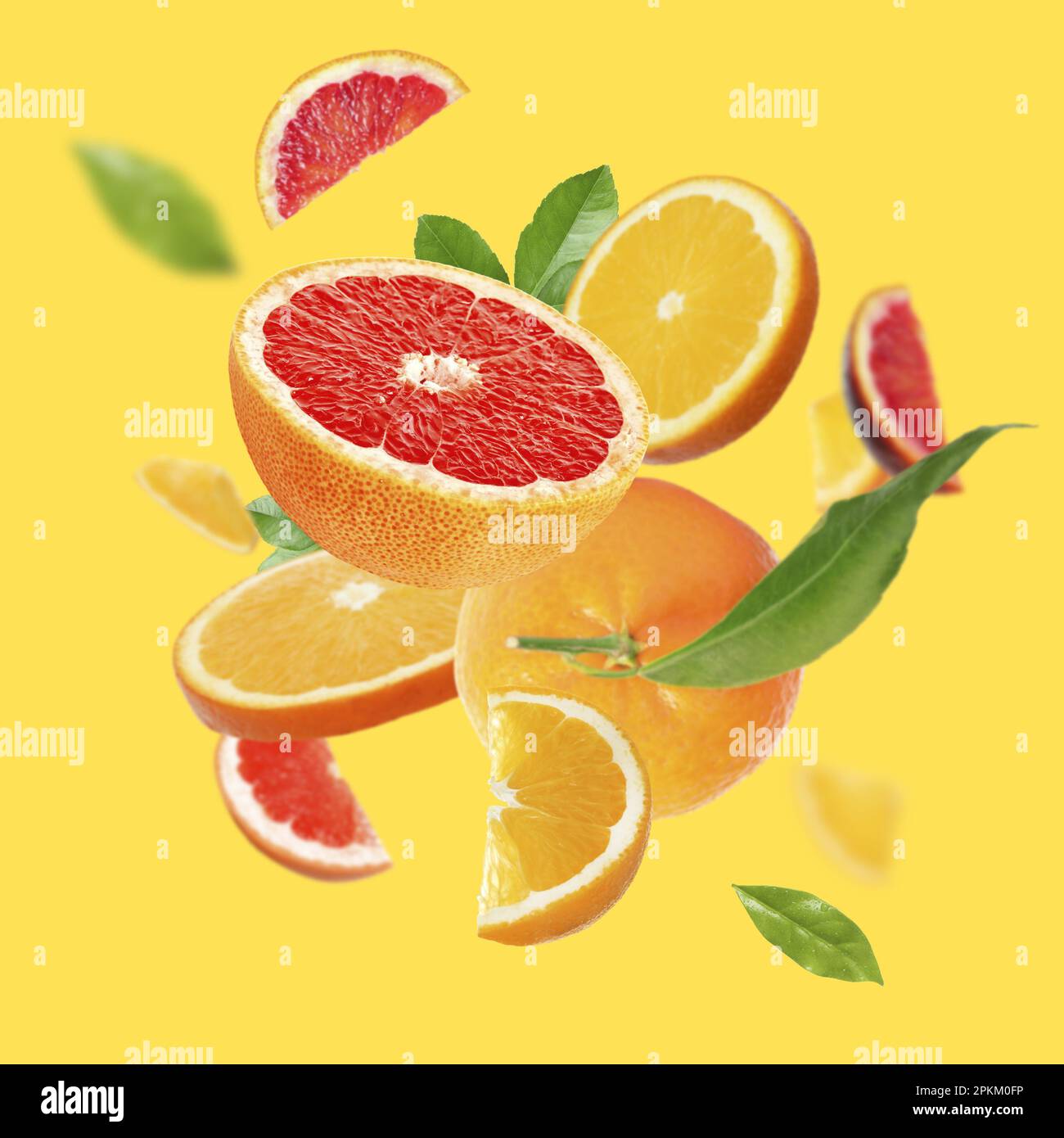 Fresh juicy citrus fruits and green leaves falling on yellow background ...