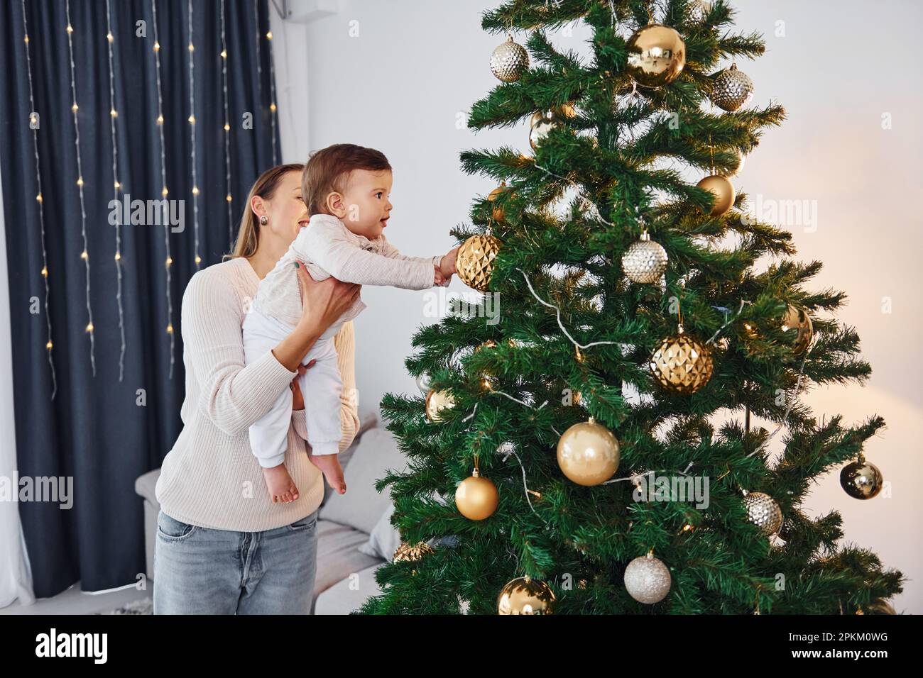 With beautiful tree. Mother with her little daughter is indoors at home together. Stock Photo