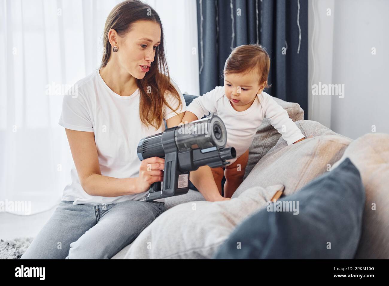 Little part of the vacuum cleaner. Mother with her little daughter is indoors at home together. Stock Photo