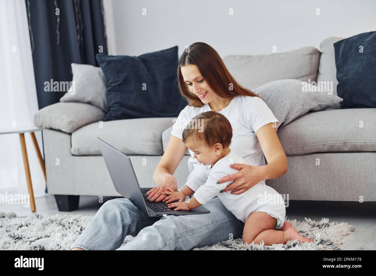Watching at the laptop. Mother with her little daughter is indoors at home together. Stock Photo