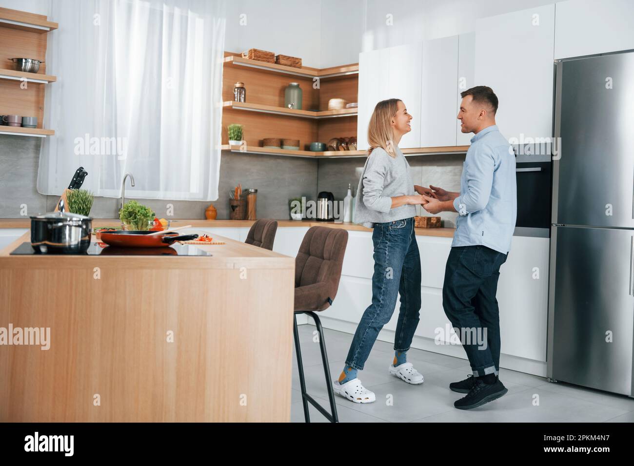 Dancing together. Couple preparing food at home on the modern kitchen. Stock Photo