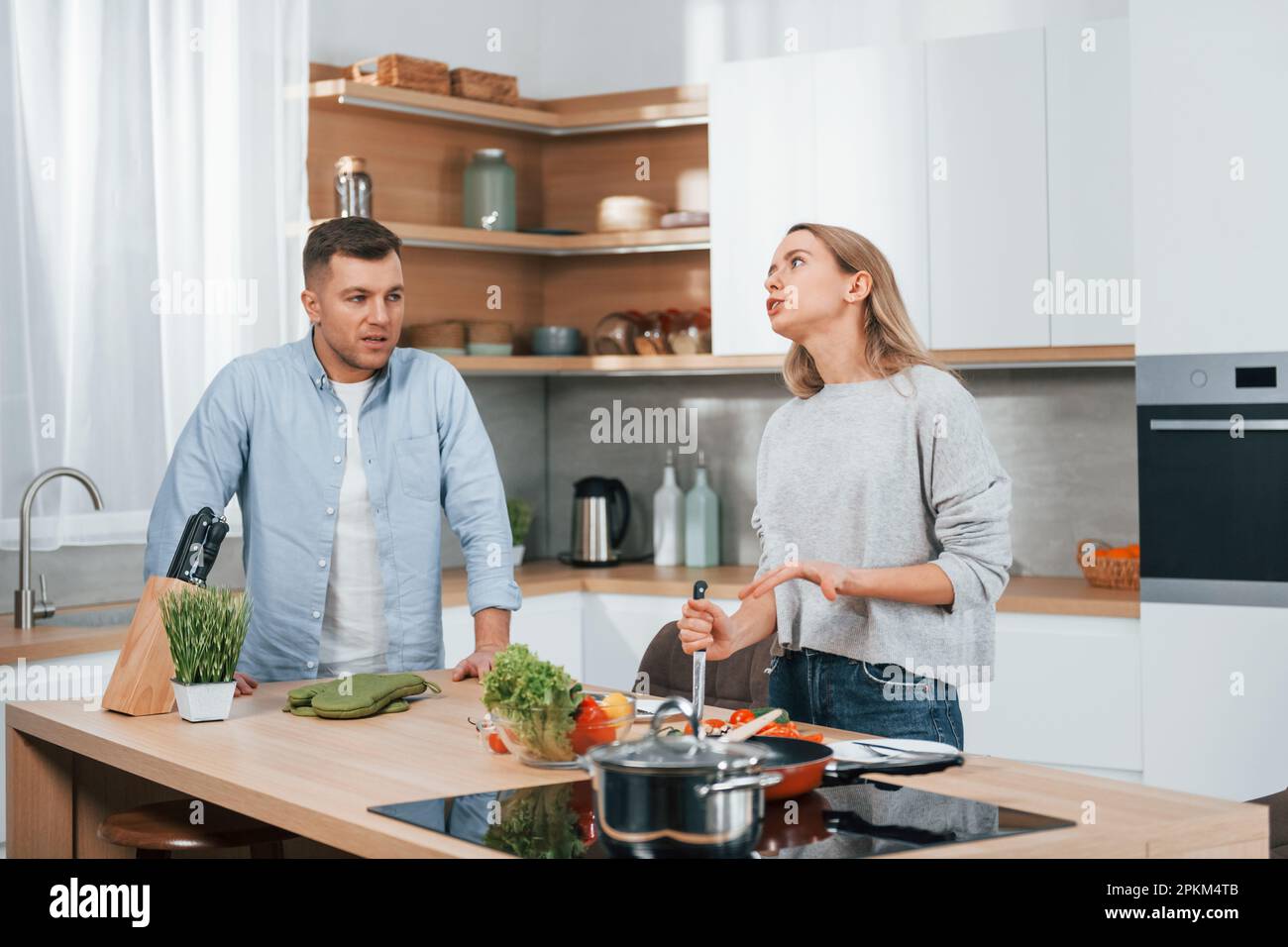 Arguing with each other. Couple preparing food at home on the modern kitchen. Stock Photo
