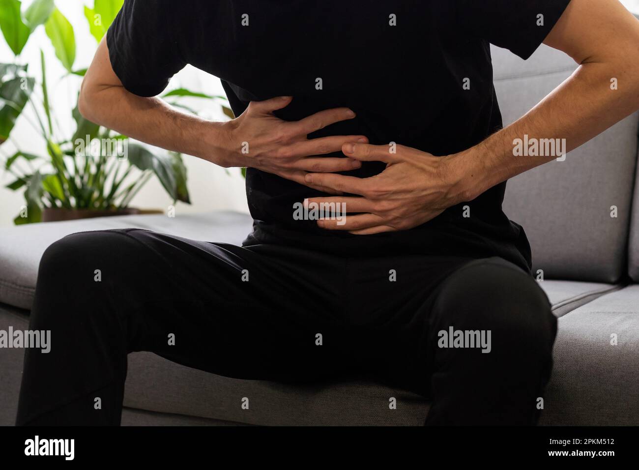 Man suffering with severe stomach pain sitting at home. Hand of mature ...