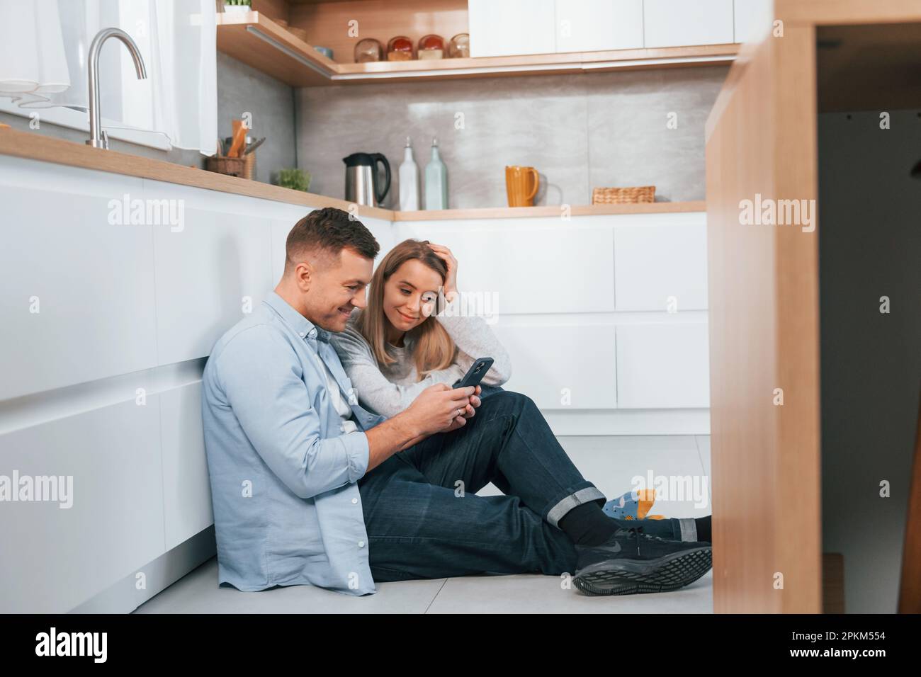 Couple sitting on the floor of modern kitchen. Stock Photo