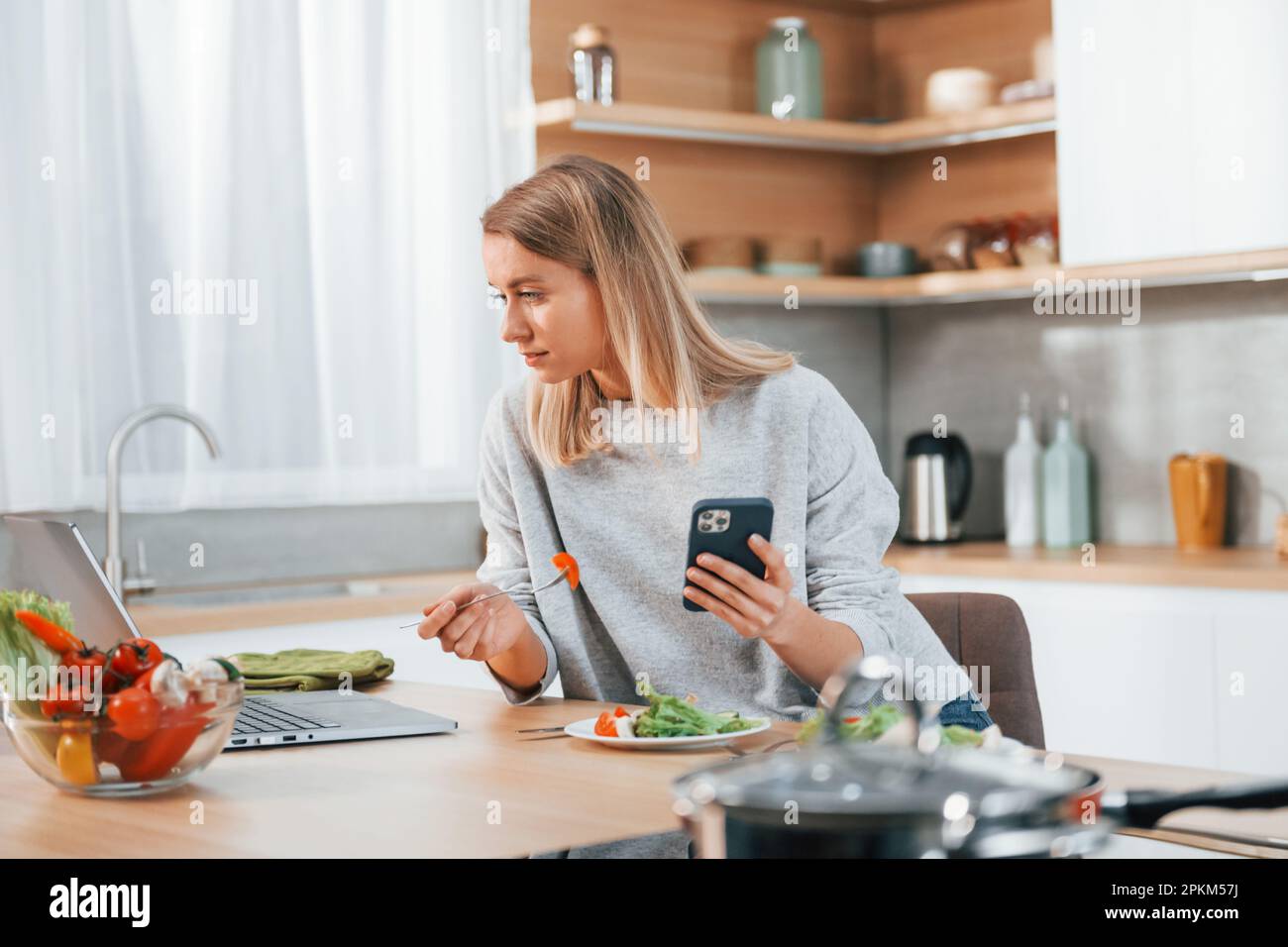Holding phone. Woman preparing food at home on the modern kitchen. Stock Photo