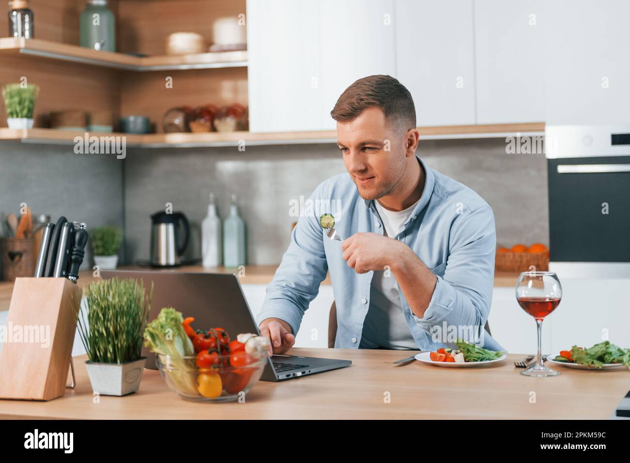 Using laptop. Man preparing food at home on the modern kitchen. Stock Photo